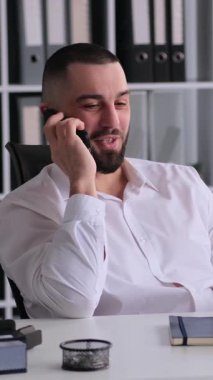 Ofiste çalışırken, orta yaşlı mutlu bir erkek işçi ya da tüketiciyle uzaktan pazarlığa ya da iş konuşmaya öncülük ediyor. Dikey video.