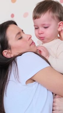 Sevecen ve sevecen genç, beyaz bir anne, kucağında ağlayan ve teselli eden bir bebek. Stres ve üzüntü kavramı. Dikey video.