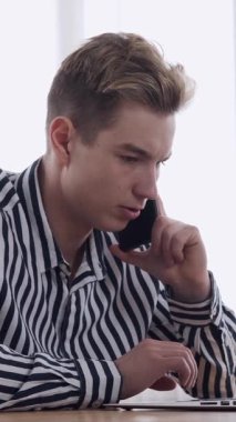 İş adamı, ofiste çalışırken, iş görüşmelerini ve iletişimi dengelemek için uzaktan bir konuşma yürütüyor. Dikey video.