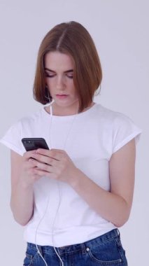 Düşünceli kadın mesajlaşmak ve beyaz arka planda internette gezinmek için telefon kullanıyor. Çevrimiçi eğlence, dijital iletişim ve bağlantı. Dikey video.