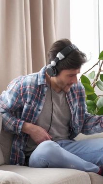 Evde gitar çalarken müzik dinleyen mutlu bir adam. Eğlencenin, eğlencenin ve eğlencenin tadını çıkarıyor. Rahatlatıcı bir atmosferde müziğin keyfini tamamen kucaklıyor. Dikey video.