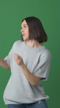 Neşeli bir kadın yeşil arka planda dans ediyor ve eğleniyor, müzik, hareket ve eğlencenin tadını çıkarırken aynı zamanda neşe ve pozitif ruh halini ifade ediyor. Dikey video.