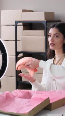 Arkadaş canlısı Kafkasyalı genç yetişkin kadın vlogger depoda çalışırken cep telefonu kullanarak çevrimiçi sosyal medya yayını yapıyor. Dikey video.