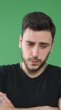 Yeşil bir arka planda baş ağrısı çeken üzgün ve sağlıksız bir adam. Yorgunluk, sıkıntı ve sağlık sorunları kavramı. Dikey video.