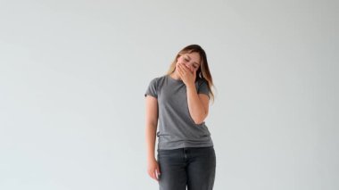 Sıkılmış ve ilgisiz, beyaz arka planda esneyen ve gerinen beyaz, genç, beyaz bir kadın. Yorgunluk, yorgunluk, tembellik kavramı.