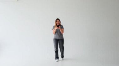 Çevrimiçi sosyal medya ve internet eğlencesinde mesajlaşmak için akıllı telefonu kullanan neşeli beyaz kadın, boş zamanlarını beyaz arka planda geçiriyor..