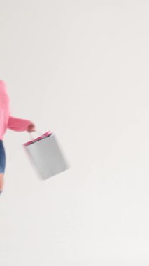 Beyaz bir arka planda alışveriş torbalarıyla yürüyen ve dans eden pozitif kadın tüketiciliği somutlaştırıyor ve heyecan satın alıyor. Dikey video.