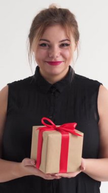 Pozitif kadın beyaz bir arkaplanda hediye kutusu veriyor. Minnettarlık, selamlama ve bayram ruhu yayıyor. Dikey video.