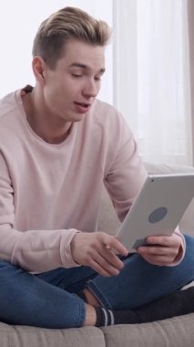 Smiley Man, evde bir tablet bilgisayarla çevrimiçi bir video görüşmesine katılıyor, boş zamanlarında keyifli bir sohbete girişiyor. Dikey video.