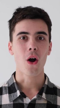 Kafkasyalı genç, şaşkın bir adamın portresi. İnançsızlığını haykırıyor ve beyaz arka planda başarıyı kutluyor. Şok ve iyi haber kavramı. Dikey video.