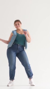 Neşeli kadın beyaz arka planda dans ederek, eğlence, dinamik hareket ve neşe göstererek zaman geçirmekten hoşlanıyor. Dikey video.