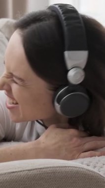 Keyifli bir kadın boş zamanın tadını çıkarıyor, evde dinlenirken müzik dinliyor. Zevk ve memnuniyet, kendini ritme kaptırır ve eğlenceli bir anın tadını çıkarır. Dikey video.