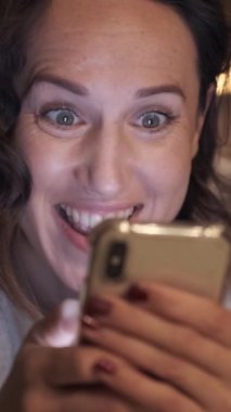 Evdeki cep telefonuyla interneti karıştıran, çevrimiçi eğlencelere dalan, bağlı kalan ve evde dinlenirken yeni içerikler keşfeden harika bir kadın. Dikey video.