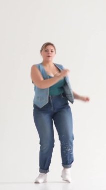 Gülen kadın dans ediyor ve beyaz bir arka planda müzik dinliyor, neşe saçıyor, parti enerjisi ve ses eğlencesi yayıyor. Dikey video.