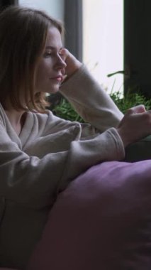 Evde boş zamanlarında akıllı telefon kullanarak çevrimiçi mesajlaşan odaklanmış bir kadın. Dijital bağlantı ve modern iletişimin kolaylığı. Dikey video.