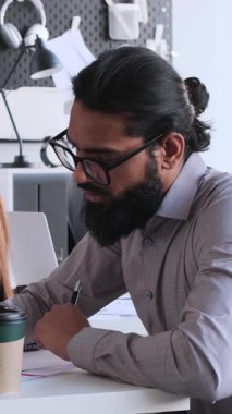 Düşünceli Arap bir adam ve beyaz bir kadın ofiste belgelerle birlikte çalışıyorlar. İş birliği konsepti. Dikey video.