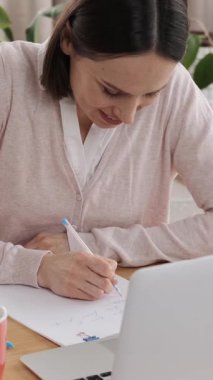 Pozitif çalışan bir ofiste çalışıyor, belgeler yazıyor ve iş geliştirmek için dizüstü bilgisayar kullanıyor. Odaklanmış ve profesyonel sorumluluklarla meşgul. Dikey video.