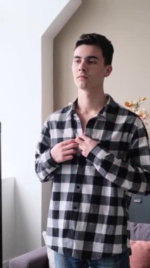 Evde aynaya bakarken konsantre olmuş, genç, beyaz, erkek gömleği. Moda ve hazırlık rutini kavramı. Dikey video.
