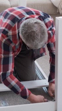Kıdemli adam evde bir masa tamir eder ya da tamir eder. Ahşap işleri, marangozluk ve ev ortamında mobilya tadilatı. Dikey video.