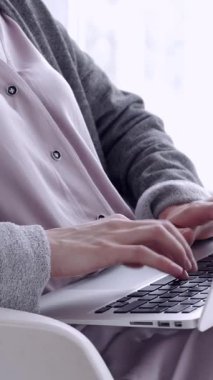 Evde dizüstü bilgisayarla çalışan odaklanmış bir kadın. İnternet iletişimi, teknoloji ve modern ev işleri. Dikey video.