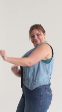 Beyaz arka planda müzik eşliğinde dans eden mutlu beyaz kadın, zevk, eğlence ve disko havası veriyor. Dikey video.