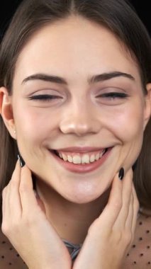 Siyah arka planda kameraya bakıp gülümseyen neşeli ve memnun bir kadının portresi. Eşsizlik ve bireysellik. Dikey video.