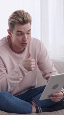 Olumlu adam evdeki tablet bilgisayarını kullanarak arkadaşlarıyla iletişim kuruyor ve boş zamanlarında çevrimiçi etkileşimden zevk alıyor. Dikey video.