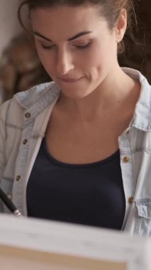 Resim stüdyosunda resim yaparken boya fırçası, palet ve resim kullanan bir kadın yaratıcı bir seansa katılıyor. Dikey video.