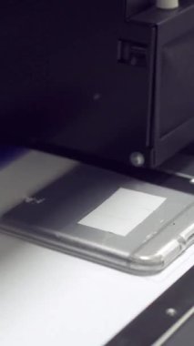 Bir ultraviyole yazıcının çalışmasını yakından çek. Teknoloji odaklı bir şirkette prodüksiyon sırasında cep telefonu kapağına detaylı tasarımlar basıyor. Dikey video.