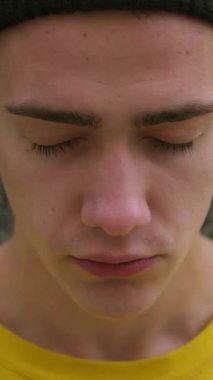 Açık havada üzgün ve üzgün genç bir beyaz adamın portresi derin duygular ve erkeksi hassasiyetini ifade ediyor. Dikey video.