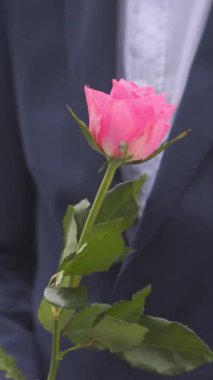 Elinde çiçekle dışarıda bir kadınla buluşmayı bekleyen bir adamın yakın çekimi. Aşk, beklenti ve romantizm. Çiçekler, bekleyiş ve özel bir an için bir randevu. Dikey video.