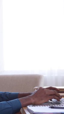 Neşeli Afro-Amerikan çalışanı evinde dizüstü bilgisayarla çalışırken sandalyeye uzanıyor. Boş zaman, iş ve rahat bir ofis ortamı. Dikey video.