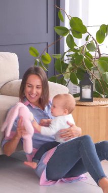 Mutlu anne ve bebek bebek evde boş vakitlerinde yumuşak bir oyuncakla oynuyorlar. Neşe, kaynaşma ve neşeli anlar. Dikey video.
