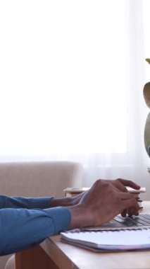 Düşünceli Afro-Amerikan uzaktan kumandalı işçi evdeki bir dizüstü bilgisayarda çalışıyor, iş teftişine ve ağ kurmaya odaklanıyor. Konsantrasyon ve profesyonellik. Dikey video.