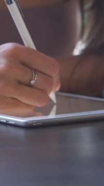 Tablet bilgisayarda resim çizen bir kadın, atölyede kıyafet tasarımları geliştiriyor. Hayal gücü, ilham ve teknolojinin moda tasarımına entegrasyonu. Dikey video.