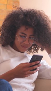 Pozitif Afro-Amerikalı kadınlar evde internet eğlencesinden ve boş zamanlarından keyif alırken telefonlarına bakıp eğleniyorlar. Dikey video.