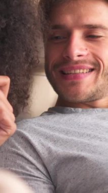Yatak odasındaki mutlu çift sabah tatili için akıllı telefon kullanıyor. Sıcaklık ve bağlılık dolu rahat bir ortamda evde sohbet etmek. Dikey video.