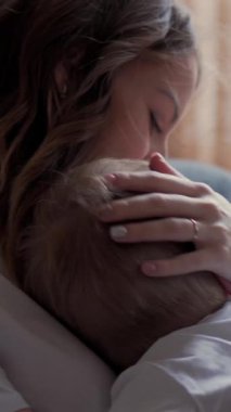 Olumlu anne ve küçük oğlu evdeki kanepede sarılıp konuşuyorlar, aile bağlarını ve sevgiyi yakalıyorlar. Dikey video.