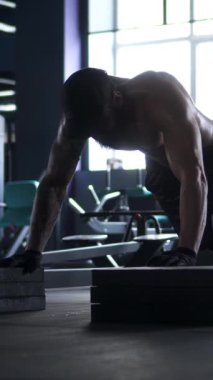 Beden eğitimi sırasında güçlü bir adam şınav çekiyor, spor salonu zindeliği ve güç gösterisi yapıyor. Egzersiz, güç ve egzersiz rutinlerine adanmışlık. Dikey video.