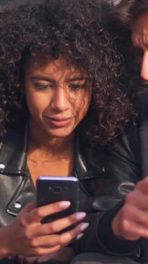 Neşeli erkek ve kadın internette internet eğlencesi için telefonları kullanarak birlikte zaman geçiriyorlar. Beraberlik ve modern rahatlama. Dikey video.