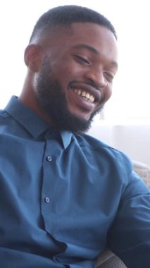 Neşeli Afro-Amerikalı adam elinde tabletle sosyal medyada mesajlaşıyor ve evde gülüyor. Neşe, iletişim ve modern teknoloji. Dikey video.