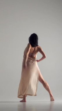 Kadın beyaz arka planda müziğe şehvetli bir dans gösterisi sunuyor, çağdaş stili sanatla harmanlıyor. Performans, gösteri ve zarafet. Dikey video.