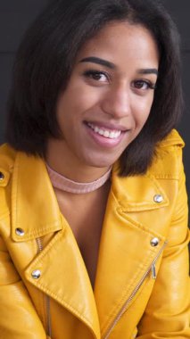 Siyah bir arka planda neşeli ve hoşnut bir Afro-Amerikan kadının portresi, keyif ve iyi bir ruh halini yansıtıyor. Dikey video.