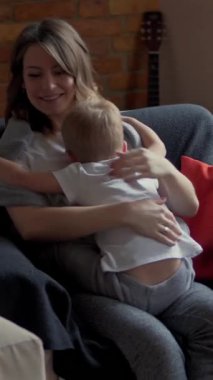 Mutlu hamile anne oğluyla oynuyor, onu evinde kucaklıyor ve öpüyor, neşe ve aile bağlarını gösteriyor. Dikey video.