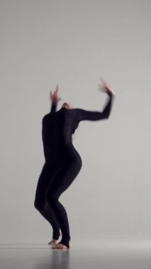 Kadın dansçı, beyaz bir arka planda, hareketli ve esneyen bir müzikle dinamik bir dans gösterisi sunar. Şovmenlik, enerji ve sanatçılık. Dikey video.