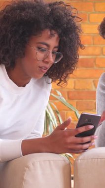 Erkek arkadaş ve kız arkadaş, hem telefon hem de tablet bilgisayar cihazlarını kullanarak evde birlikte vakit geçirmenin ve eğlencenin tadını çıkarıyorlar. Dikey video.