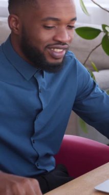 Afrikalı Amerikalı bir çalışan bir dizüstü bilgisayarda çalışıyor ve ev ofisinde notlar alıyor. İstihdam, eğitim ve uzak bir çalışma ortamında odaklanma. Dikey video.