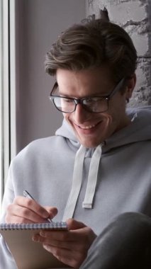 Hevesli erkek ve kadın birlikte oturur, bir not defterine yazarlar, heyecanlı bir şekilde evde ortak bir gelecek planlarlar. Ortaklık, beklenti ve ortak hayaller. Dikey video.