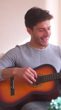 Mutlu erkek arkadaş ve kız arkadaş evde boş zamanlarında birlikte gitar çalıp şarkı söylemekten ve müzik anlarını paylaşmaktan hoşlanırlar. Dikey video.