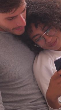 Keyifli erkek ve kadın evdeki kanepede birlikte dinlenirken boş zamanlarında online eğlence için telefon kullanıyorlar. Dikey video.